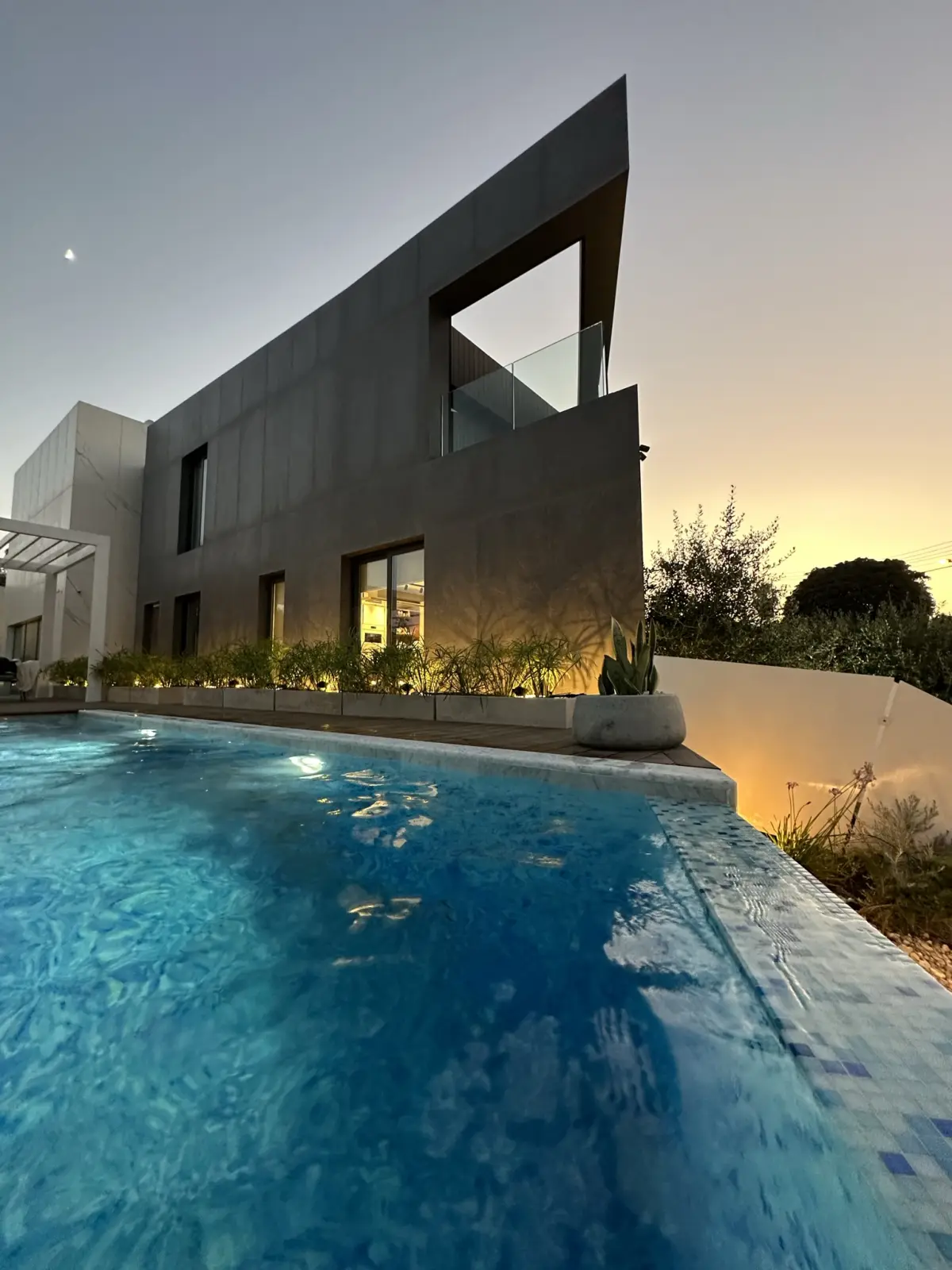 Pool and dark stone facade of the Madliena villa at dusk